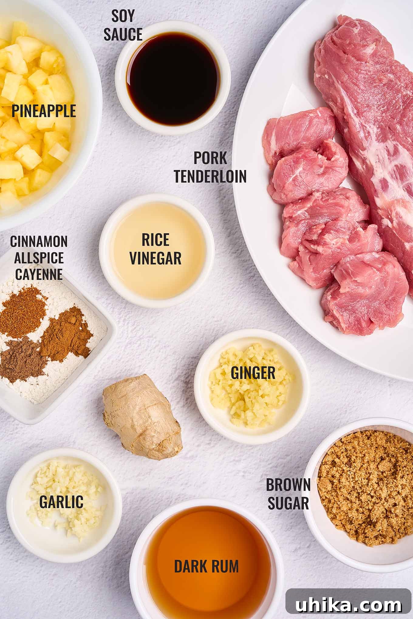Island-Style Pineapple Pork Skillet 3 A labeled overhead view of the ingredients for Caribbean pineapple pork with rum sauce, including pork tenderloin, fresh pineapple, dark rum, brown sugar, and a selection of aromatic spices like ginger, cinnamon, and allspice.