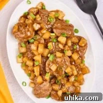 An oval serving platter of Caribbean-style pineapple pork with tender pork medallions, pineapple chunks, and scallions in a sweet-savory rum sauce.