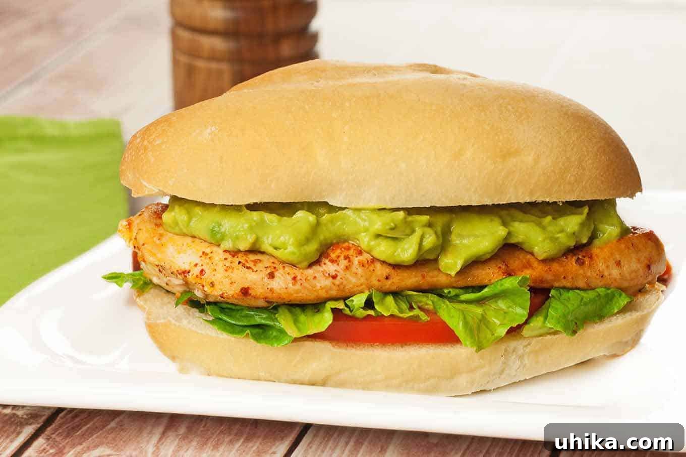 A pan-seared chicken sandwich with avocado mayo, lettuce, and tomato on a sandwich roll, a pepper mill in the background.