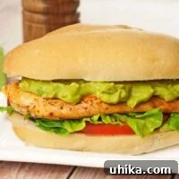 A pan-seared chicken sandwich with avocado mayo, lettuce, and tomato on a sandwich roll, a pepper mill in the background.