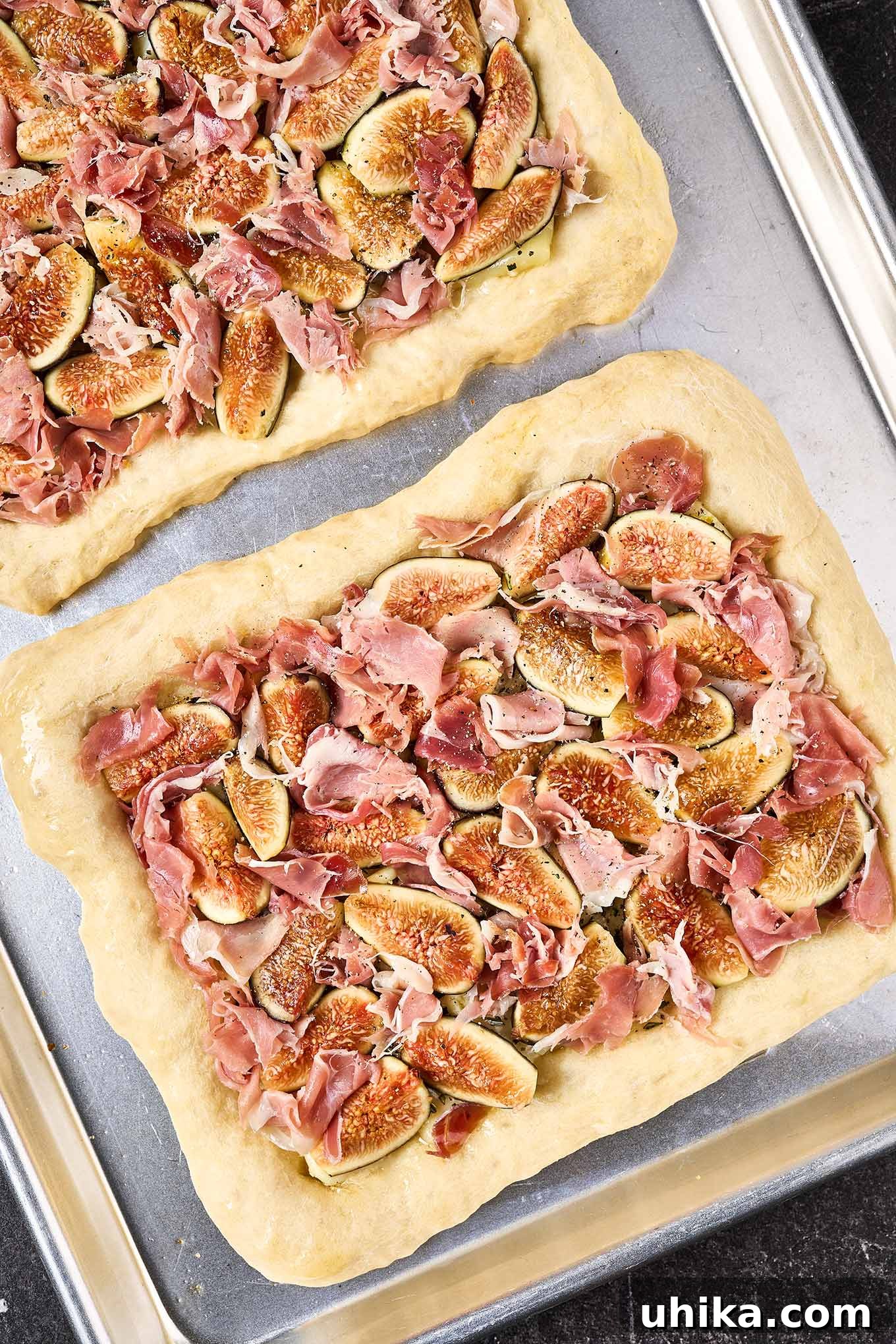 Gourmet Fig Prosciutto Brie Pizza 4 A recipe prep photo showing two pre-baked pizza crusts topped with brie, quartered figs, and prosciutto, ready for final baking. The ingredients are evenly distributed for a perfect bake.