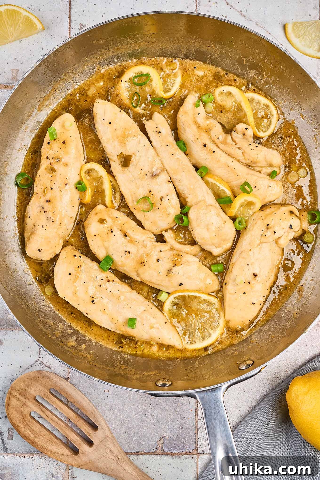 Crispy Lemon Pepper Chicken Strips 4 Pan seared chicken tenderloins in a stainless steel frying pan with lemon pepper pan sauce, garnished with lemon slices, and chopped scallions.