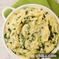 An overhead view of a white casserole filled with creamy mashed potatoes mixed with sautéed kale, sweet onion, and scallions (colcannon), and a serving spoon.