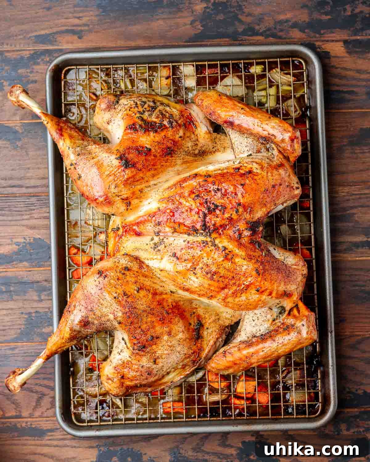 Flatter, Faster, Flawless: The Spatchcock Turkey 2 Overhead shot of roasted spatchcock turkey on wire rack lined baking sheet, garnished with fresh herbs.