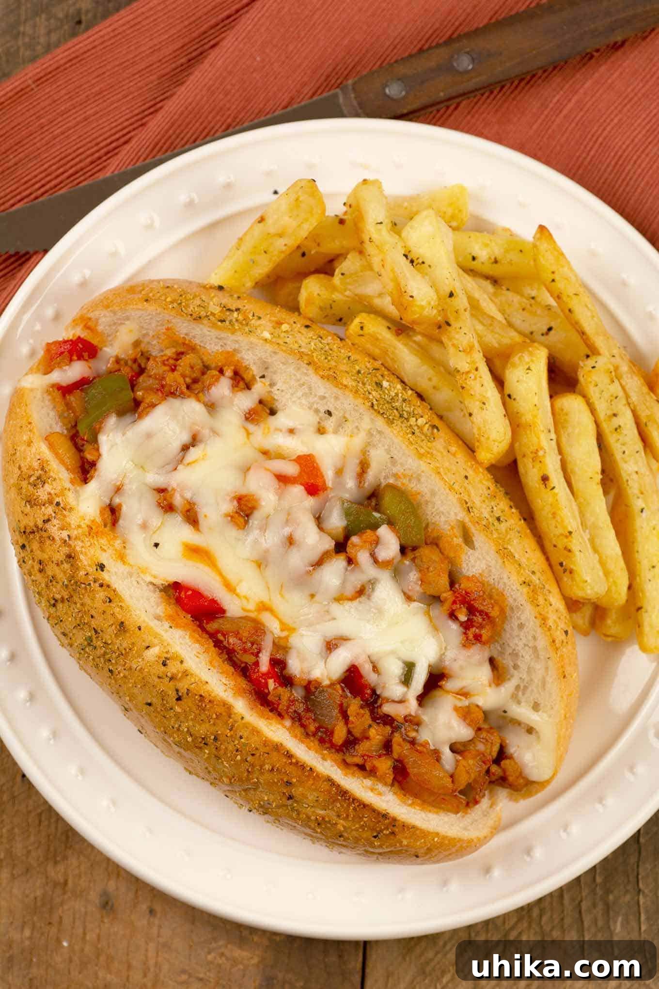The Italian Job Sandwich 2 A plate with a sub roll filled with a sloppy-Joe style mix of crumbled Italian sausage, green pepper, tomato sauce, and melted mozzarella, fries on the side.