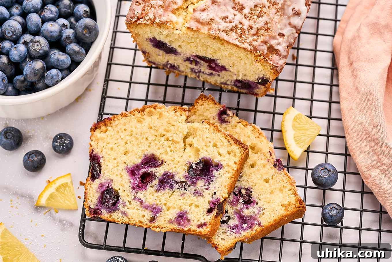 Luscious Lemon Blueberry Loaf 5 A tantalizing close-up shot of a freshly sliced lemon blueberry loaf cake, showcasing its incredibly moist crumb studded generously with vibrant, juicy blueberries. The cake rests invitingly on a wire cooling rack, ready to be enjoyed.