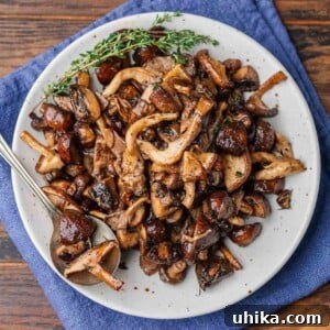 Golden Roasted Mushrooms 8 Featured image of roasted mushrooms with thyme garnish in white plate on blue napkin.