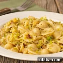A plate of orecchiette pasta tossed with sautéed shredded Brussels sprouts and bacon, a fork and napkin in the background.