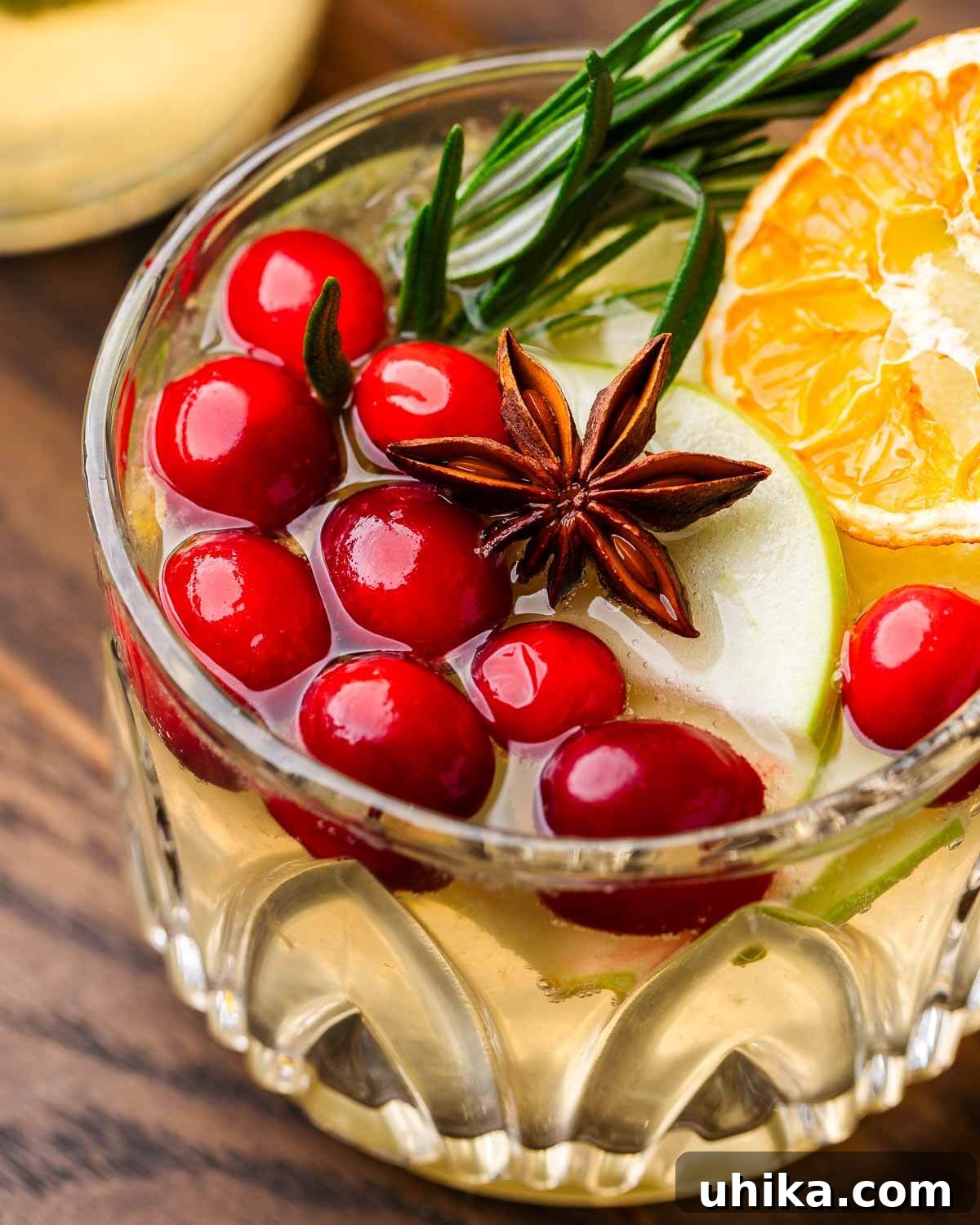 Spiced Christmas Sangria 2 A beautifully arranged glass of Christmas Sangria, featuring vibrant red cranberries, a star anise pod, and a sprig of fresh rosemary, set against a cozy holiday backdrop. This festive drink is perfect for holiday celebrations.