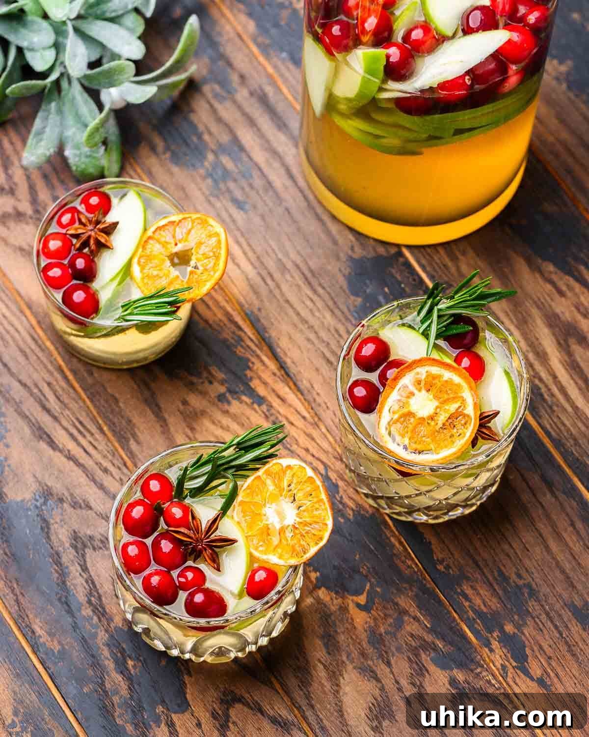 Spiced Christmas Sangria 5 A festive holiday table adorned with three glasses of vibrant Christmas Sangria, alongside a matching pitcher, all ready for a celebration. The rich red and green hues create a joyful atmosphere.