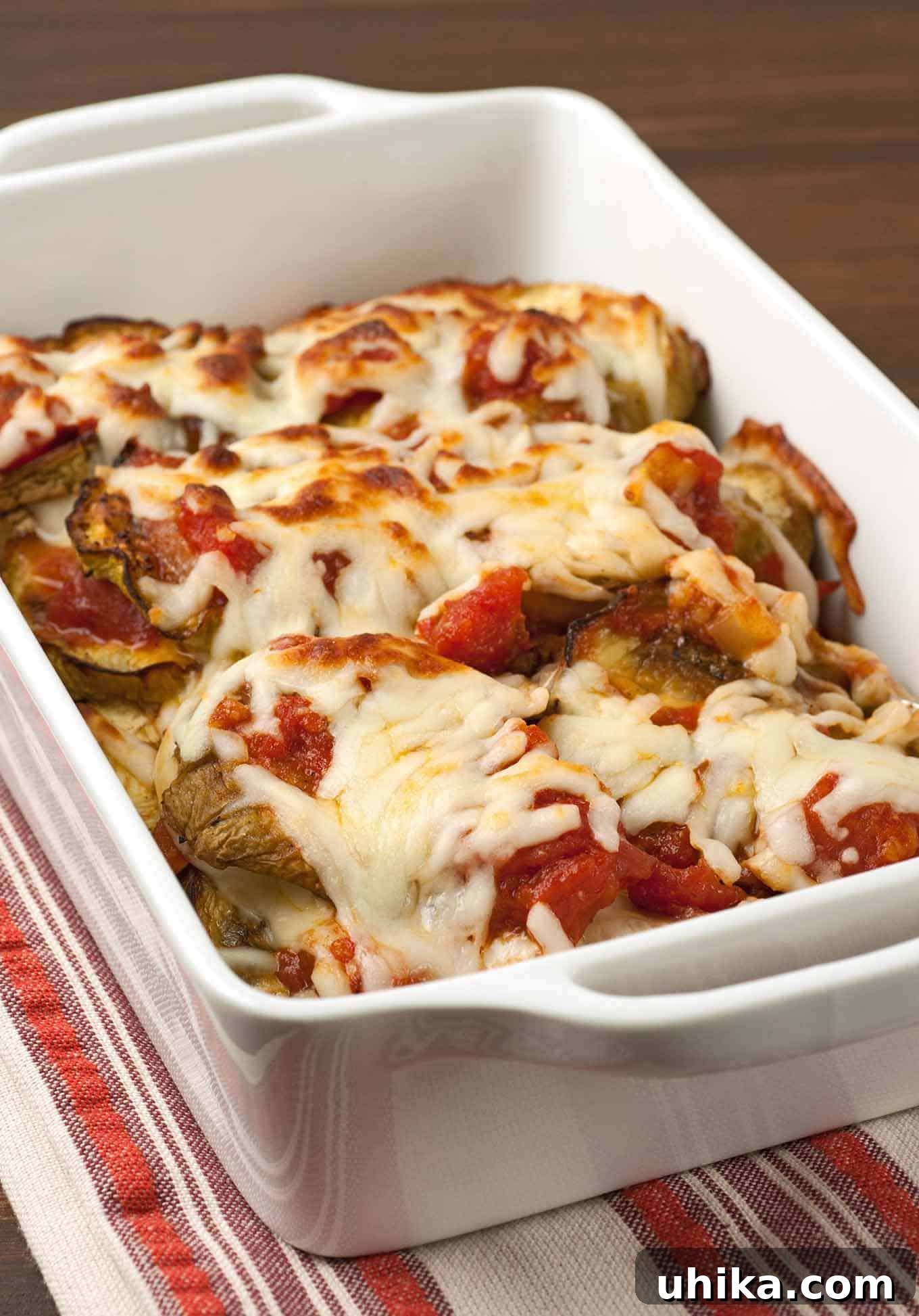 Hearty Italian Eggplant Bake 2 Delicious Baked Italian-style eggplant casserole in a white dish, layered with rich tomato sauce and melted provolone and mozzarella cheeses, ready to be served.