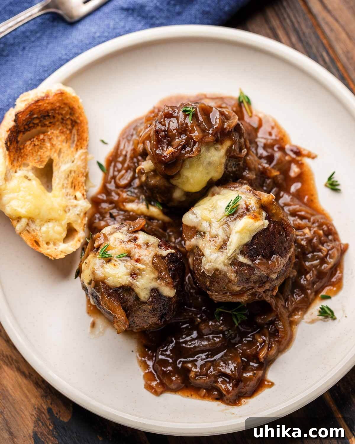 Bistro French Onion Meatballs 7 A perfectly plated dish showcasing three French onion meatballs, generously covered in rich caramelized onion sauce and melted Swiss cheese, served with a side of toasted cheesy baguette on a white plate.