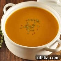 White ceramic bowl filled with smooth roasted butternut squash and chestnut soup, garnished with fresh thyme on top.