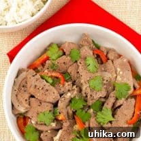 Fragrant Vietnamese Garlic and Black Pepper Stir Fry 3 A serving bowl of stir-fried garlic and black pepper beef with strips of red bell pepper and sliced onion, and a garnish of cilantro leaves, a bowl of white rice for serving.