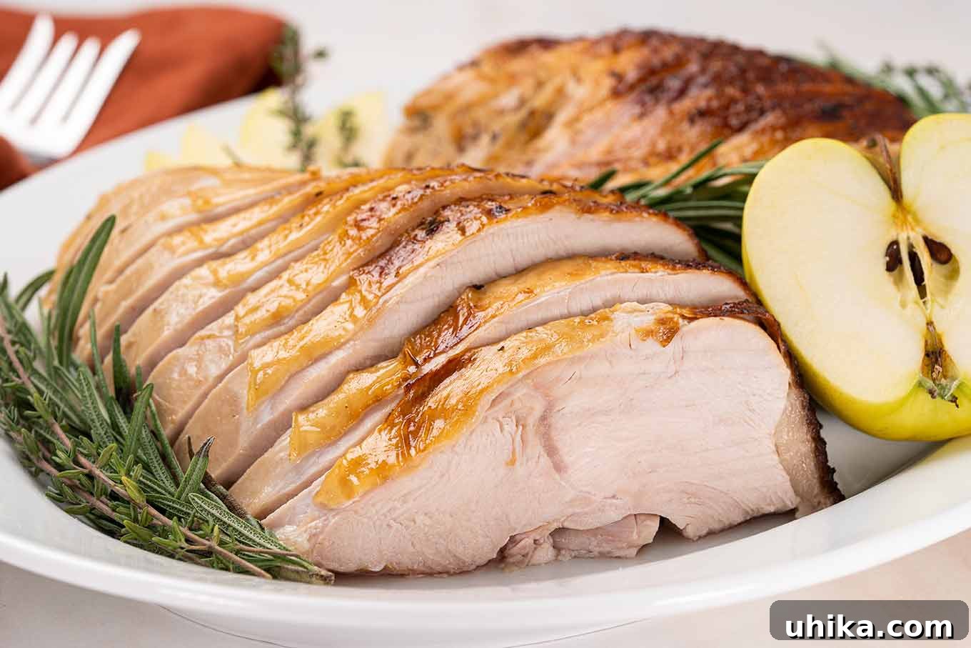 Sweet & Savory Apple Cider Turkey Breast 4 Juicy slices of apple cider brined turkey breast with golden brown skin on a serving platter with fresh rosemary, thyme, and an apple.