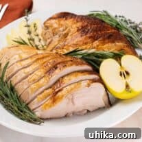 Sliced apple cider brined turkey breast on an oval serving platter garnished with a cut golden delicious apple, fresh rosemary, and fresh thyme.