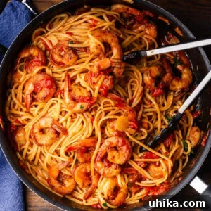 Shrimp fra diavolo in black pan with tongs.