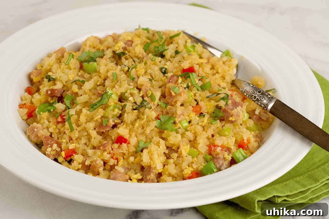 Light Cauliflower Fried Rice 3 A serving of riced cauliflower fried rice, garnished with chopped cilantro, served in a shallow bowl with a fork.