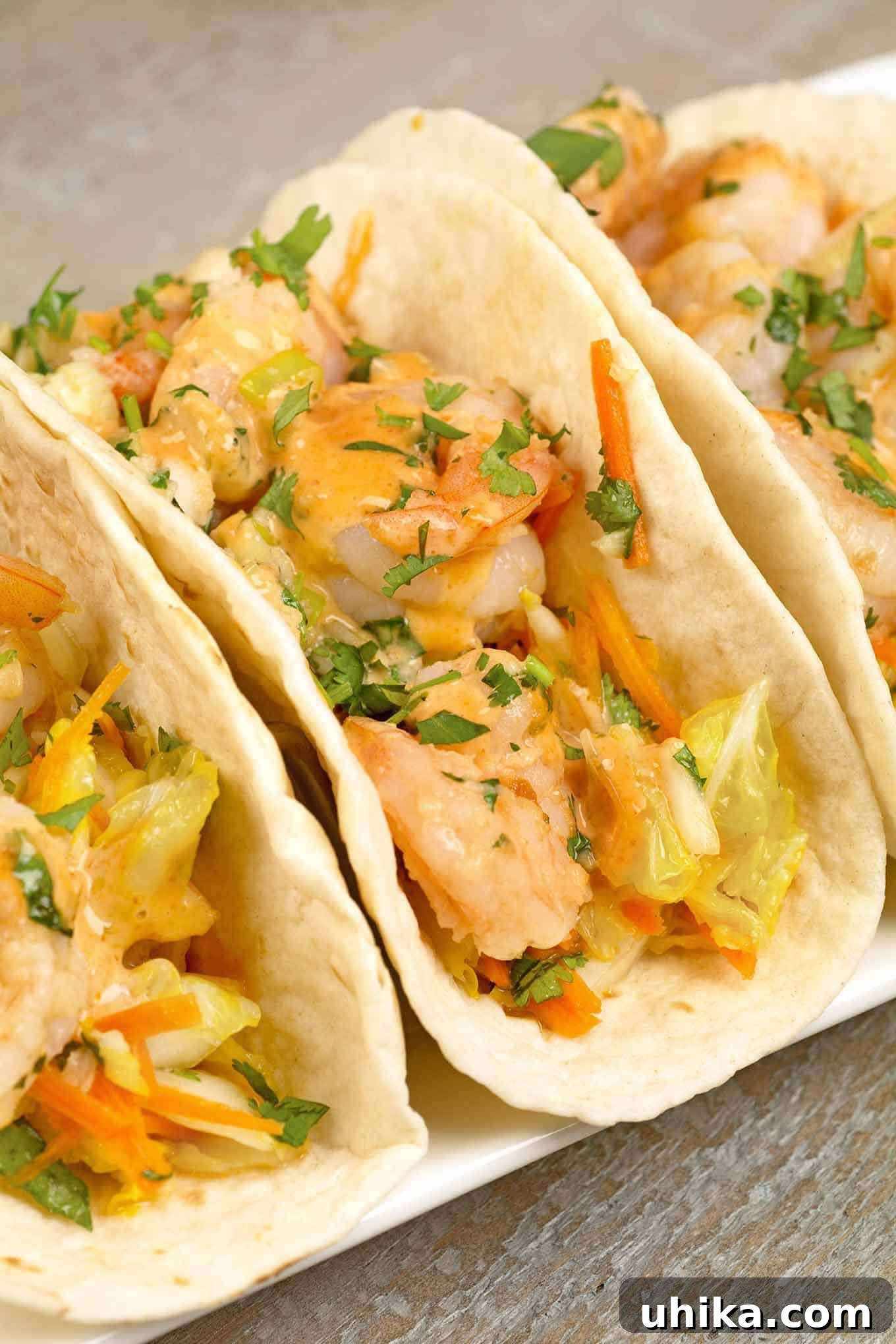 Asian Kick Shrimp Tacos 3 A closeup view of soft tacos filled with stir-fried shrimp and napa cabbage slaw, drizzled with sriracha mayo and garnished with fresh cilantro, highlighting the vibrant colors and appealing textures.