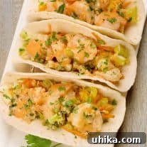 An overhead view of soft flour tortillas filled with crisp napa cabbage slaw, jumbo shrimp stir-fried with garlic and ginger, and a garnish of chopped cilantro.