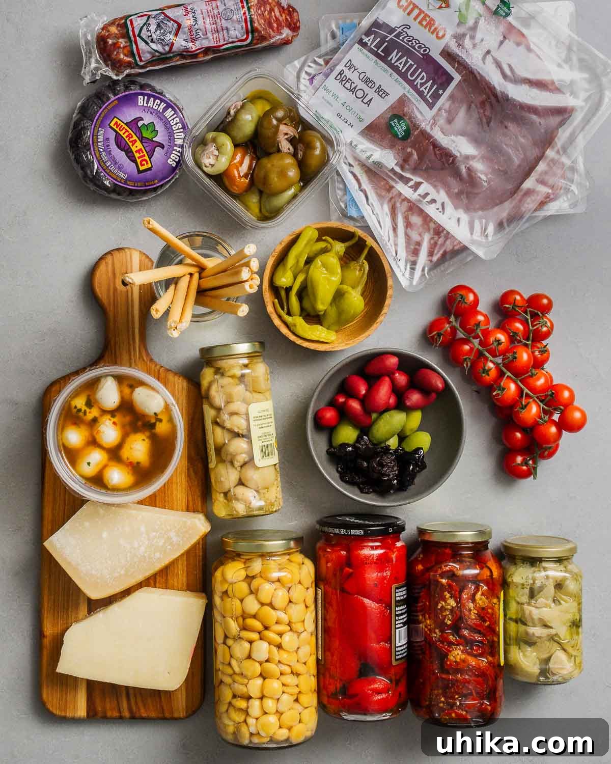 Crafting the Ultimate Antipasto Board 3 A vibrant selection of antipasto ingredients laid out: salami, figs, stuffed cherry peppers, various cured meats, breadsticks, mozzarella balls, assorted cheeses, pickled mushrooms, roasted red peppers, sun-dried tomatoes, artichoke hearts, olives, and cherry tomatoes.