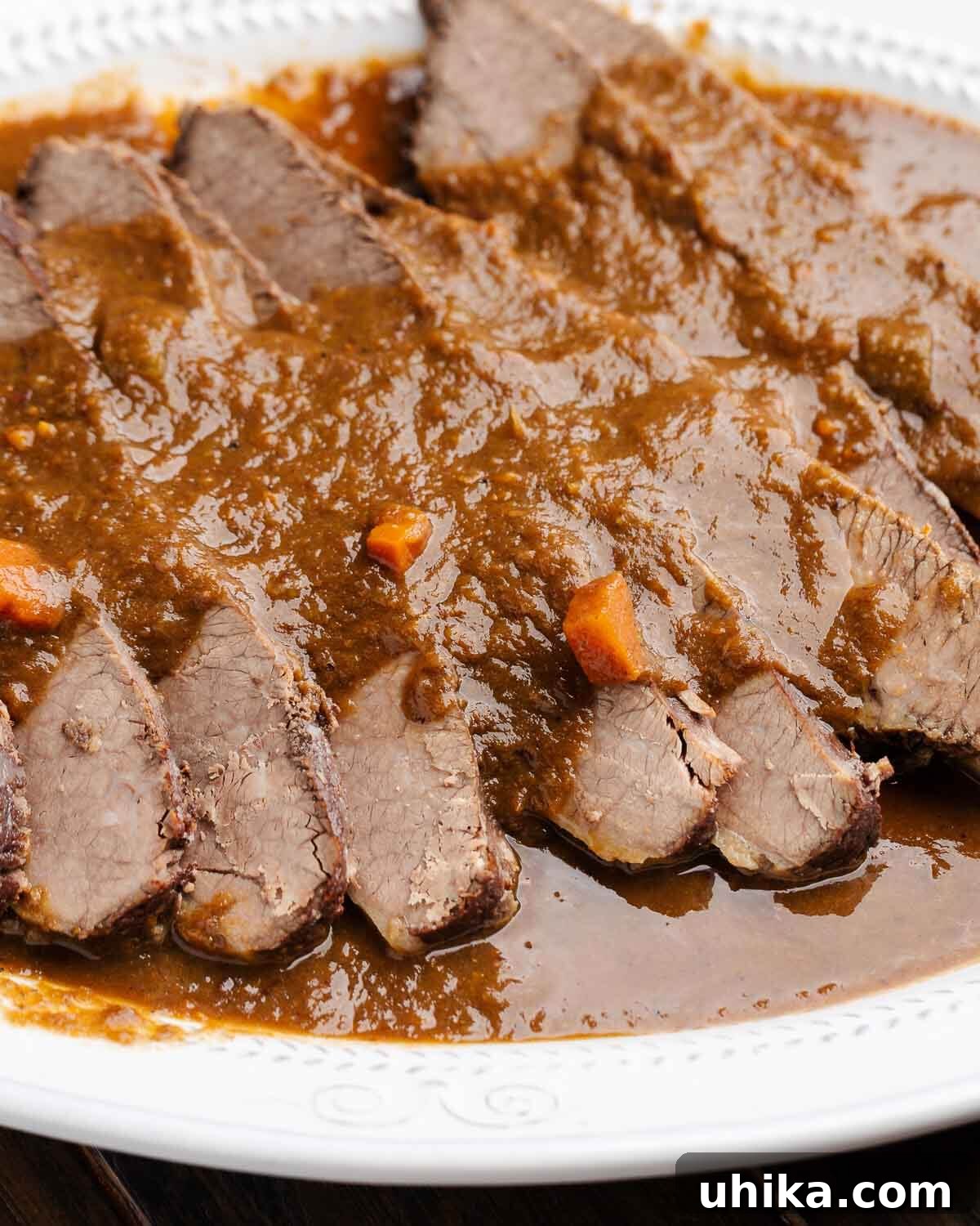 White platter with sliced brisket pieces with wine sauce.