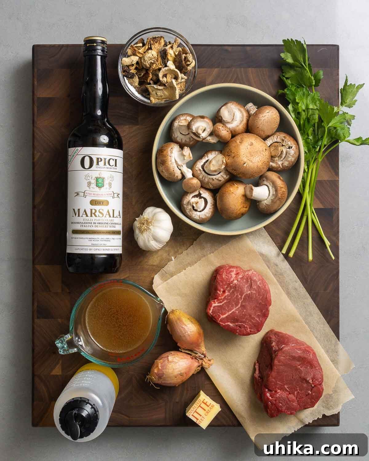 Rich Marsala-Braised Beef 3 A curated selection of fresh and pantry ingredients for Beef Marsala, including marsala wine, an assortment of mushrooms, fresh parsley, garlic cloves, rich beef stock, olive oil, shallots, unsalted butter, and two premium filet mignon steaks.