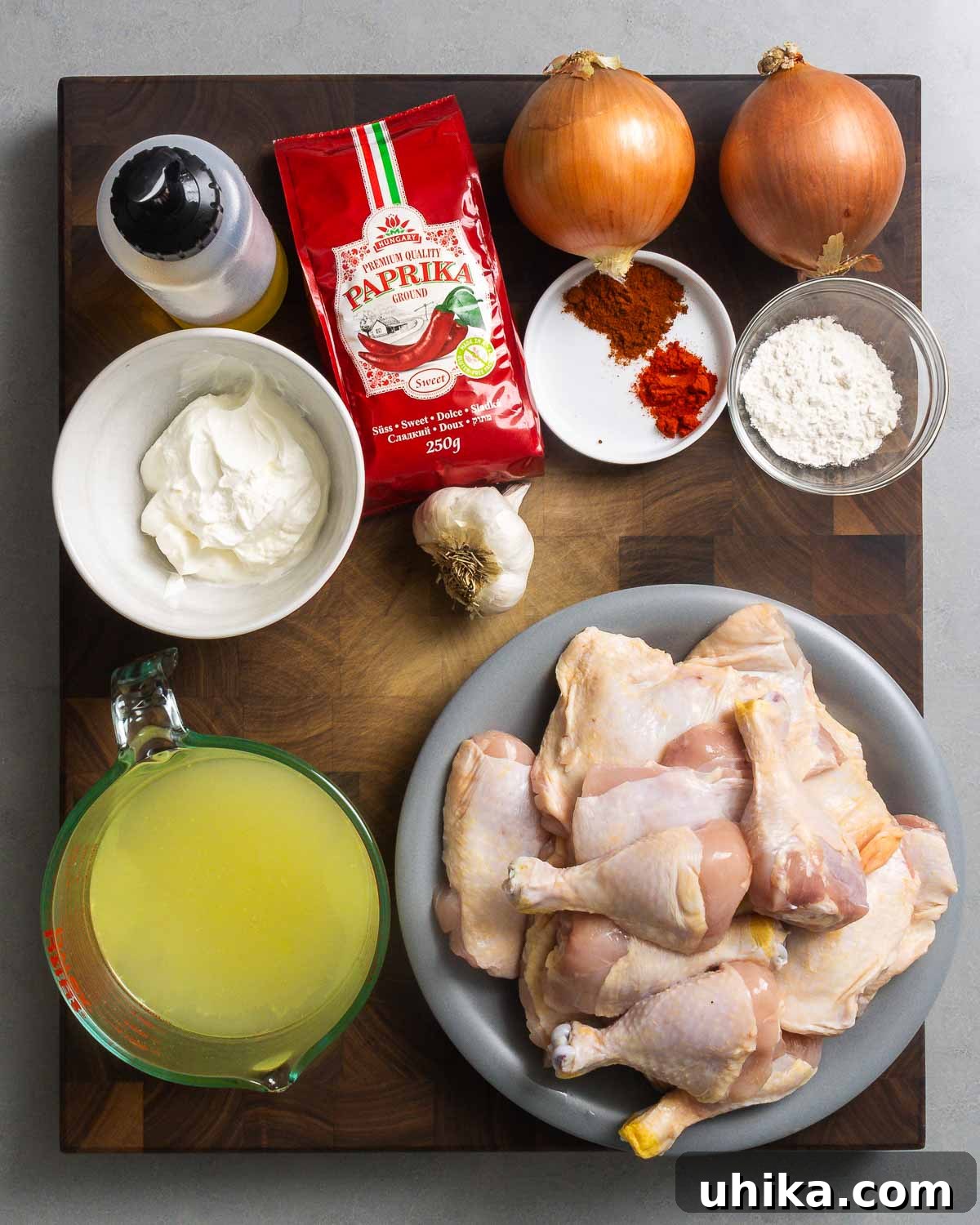 Hearty Paprikash Chicken with Cloud-Like Dumplings 3 Ingredients shown: olive oil, Hungarian paprikas, onions, flour, sour cream, chicken stock, garlic, and plate of chicken pieces.