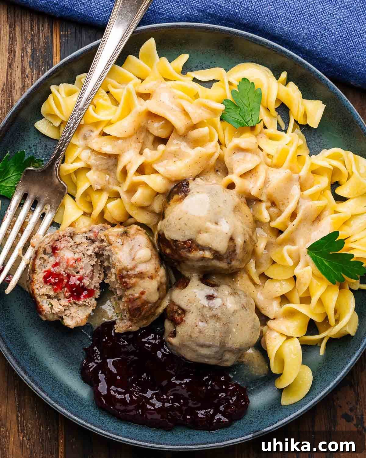 Nordic Meatball Delight 7 A plate of golden-brown Swedish meatballs generously covered in creamy gravy, served over a bed of egg noodles with a vibrant red dollop of lingonberry jam on the side.