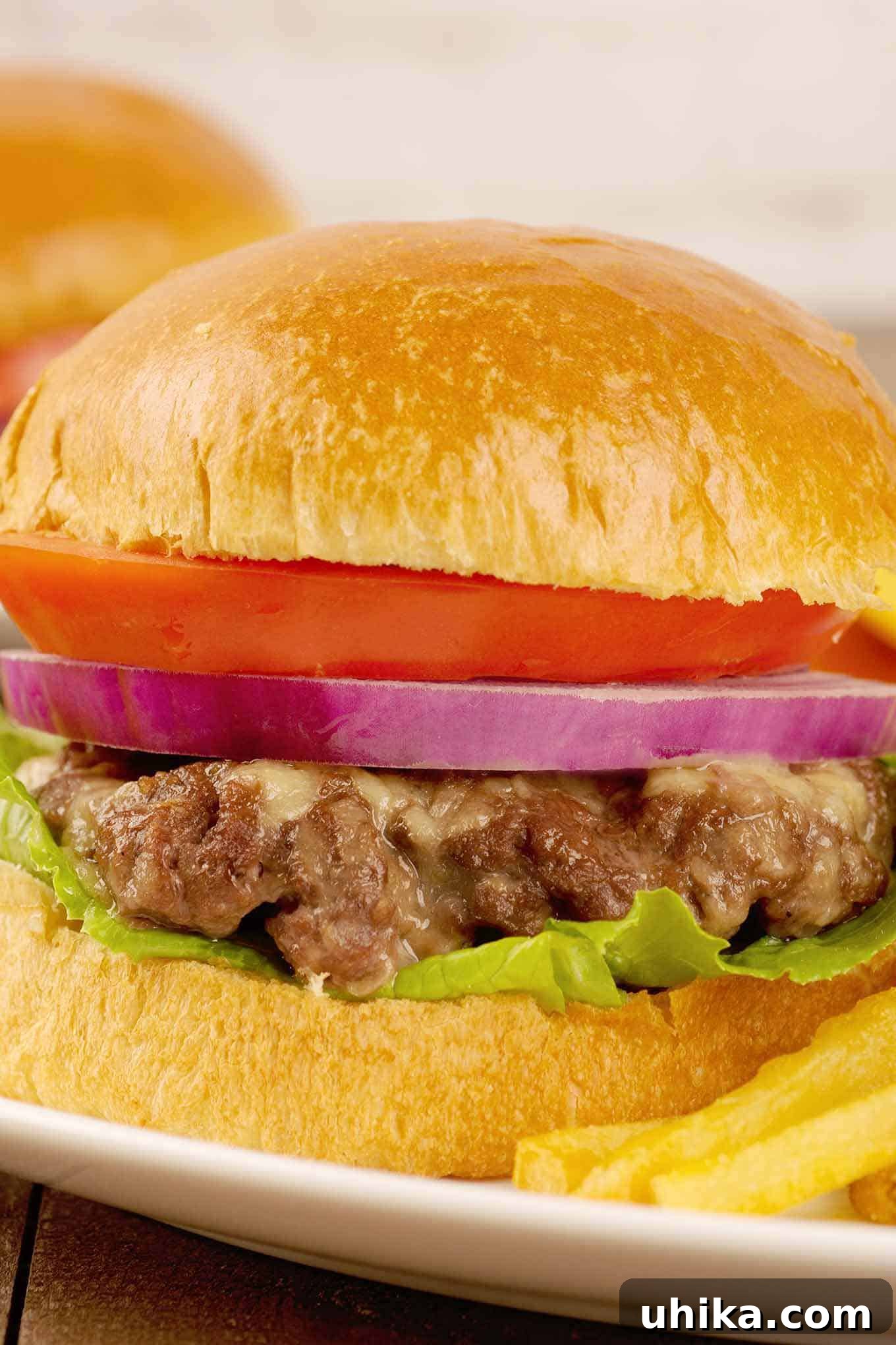 Oven Baked Cheeseburgers 2 A close side view of an oven-baked cheeseburger stacked with lettuce, tomato, and onion, with the melted cheese inside the burger clearly visible. A perfect, juicy, homemade oven-baked burger.