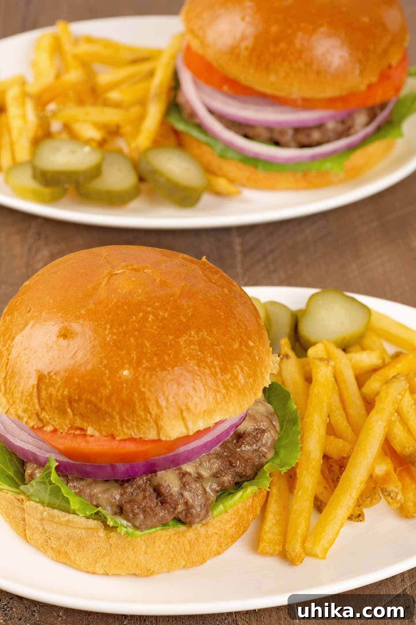 Oven Baked Cheeseburgers 4 A overhead view of two plated servings of oven-baked cheeseburgers with crispy French fries and pickle slices on the side. A complete and satisfying meal.