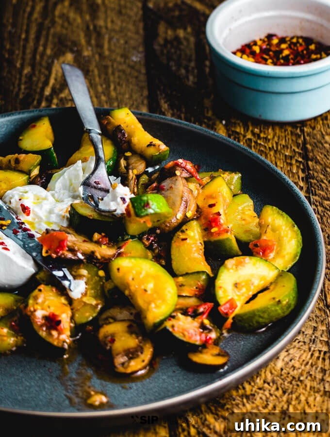 Sauteed Zucchini and Mushrooms with Burrata Ready to Serve A beautifully plated serving of sauteed zucchini and mushrooms with burrata, garnished with fresh basil, set on a wooden table with a fork.
