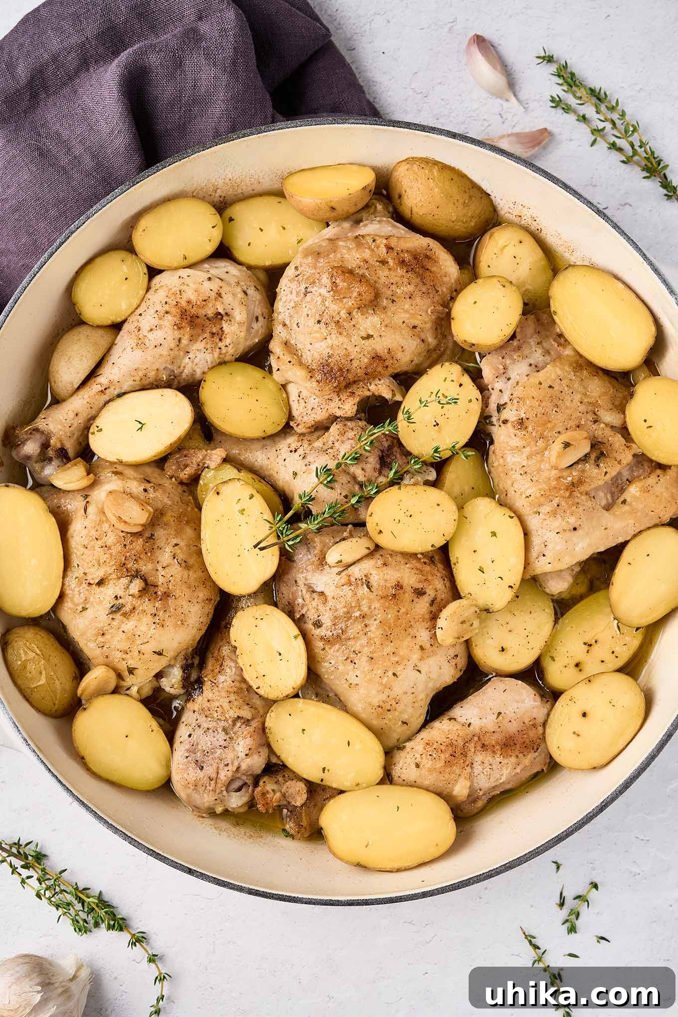 Hearty Braised Chicken and Potatoes 2 Braised chicken legs with baby potatoes, garlic, and thyme in a large pan after cooking.