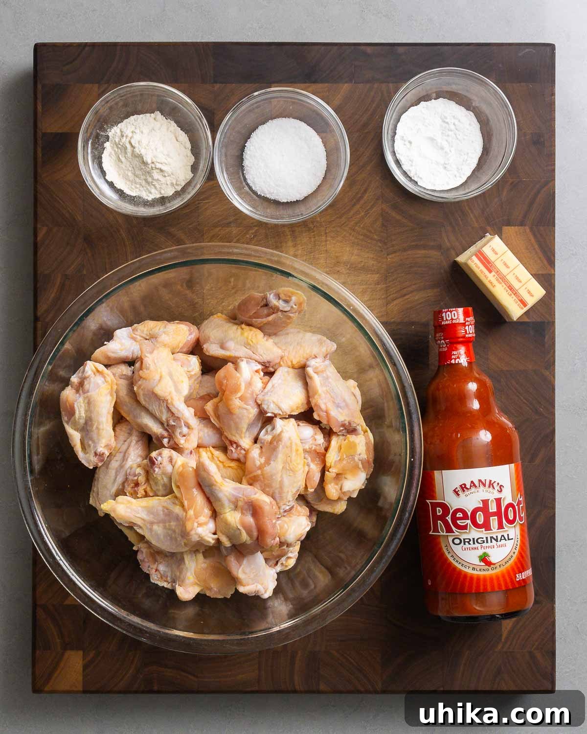 Buffalo Wing Perfection 3 Ingredients for buffalo wings laid out: all-purpose flour, Diamond Crystal kosher salt, aluminum-free baking powder, unsalted butter, party chicken wings, and Frank's RedHot sauce.