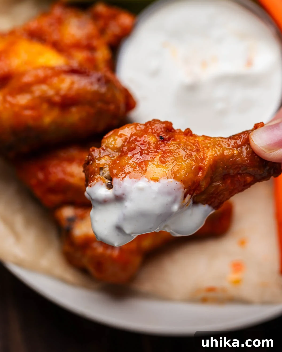 A hand holds a buffalo wing, freshly dipped in a generous amount of creamy blue cheese dressing.