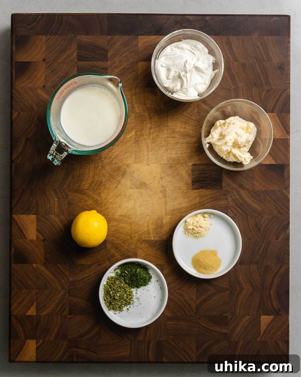 Velvet Buttermilk Ranch 3 Ingredients for buttermilk ranch dressing: buttermilk, mayonnaise, sour cream, lemon, granulated garlic, onion powder, dried parsley, and dried dill displayed on a wooden surface.