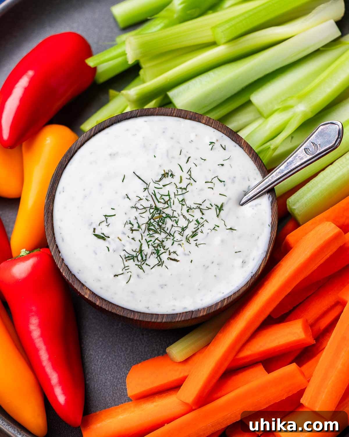Velvet Buttermilk Ranch 4 Grey plate with a small bowl of creamy ranch dressing surrounded by an assortment of fresh-cut vegetables like carrots, celery, and bell peppers.