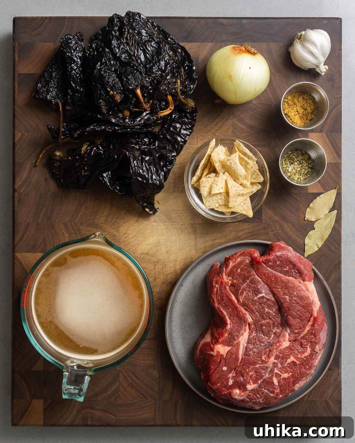 Crimson Beef Chili 3 Ingredients shown: dried chile peppers, onion, garlic, cumin, oregano, tortillas, bay leaves, beef stock, and beef chuck.