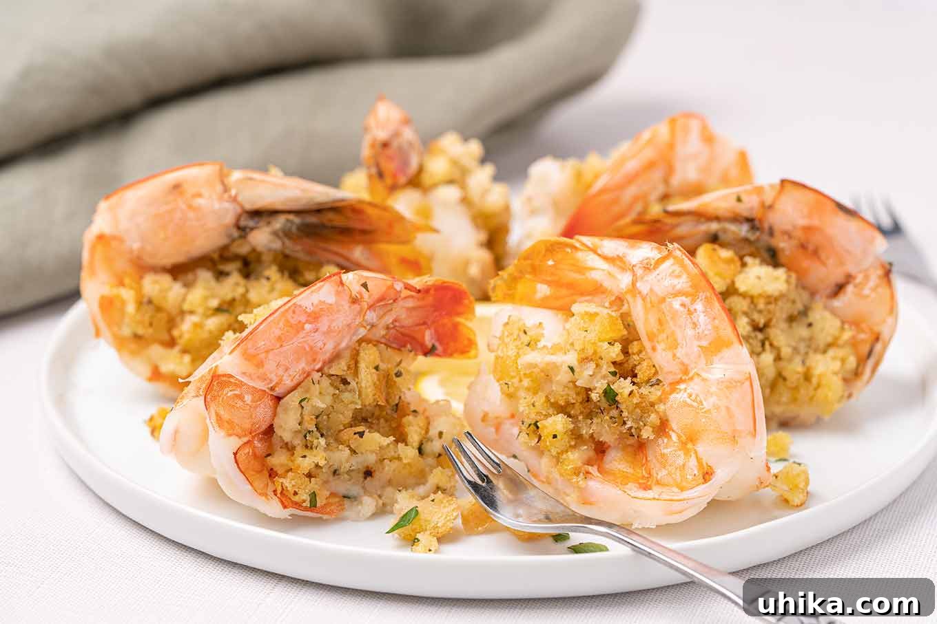 Oven-Baked Shrimp Treasures 4 A side view of a serving of baked stuffed shrimp showing the buttery fresh breadcrumb topping with herbs, a seafood fork on the plate. This recipe is a New England classic reimagined.