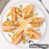 An overhead view of a round white plate filled with baked stuffed colossal shrimp with seafood forks and lemon slices for garnish.
