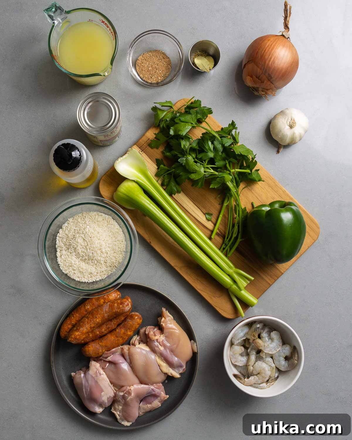 Creole Comfort 3 A flat lay of all the ingredients required for Jambalaya, including chicken stock, Cajun seasoning, various spices, onion, garlic, tomato sauce, olive oil, celery, bell pepper, fresh parsley, rice, Andouille sausage, chicken thighs, and shrimp.