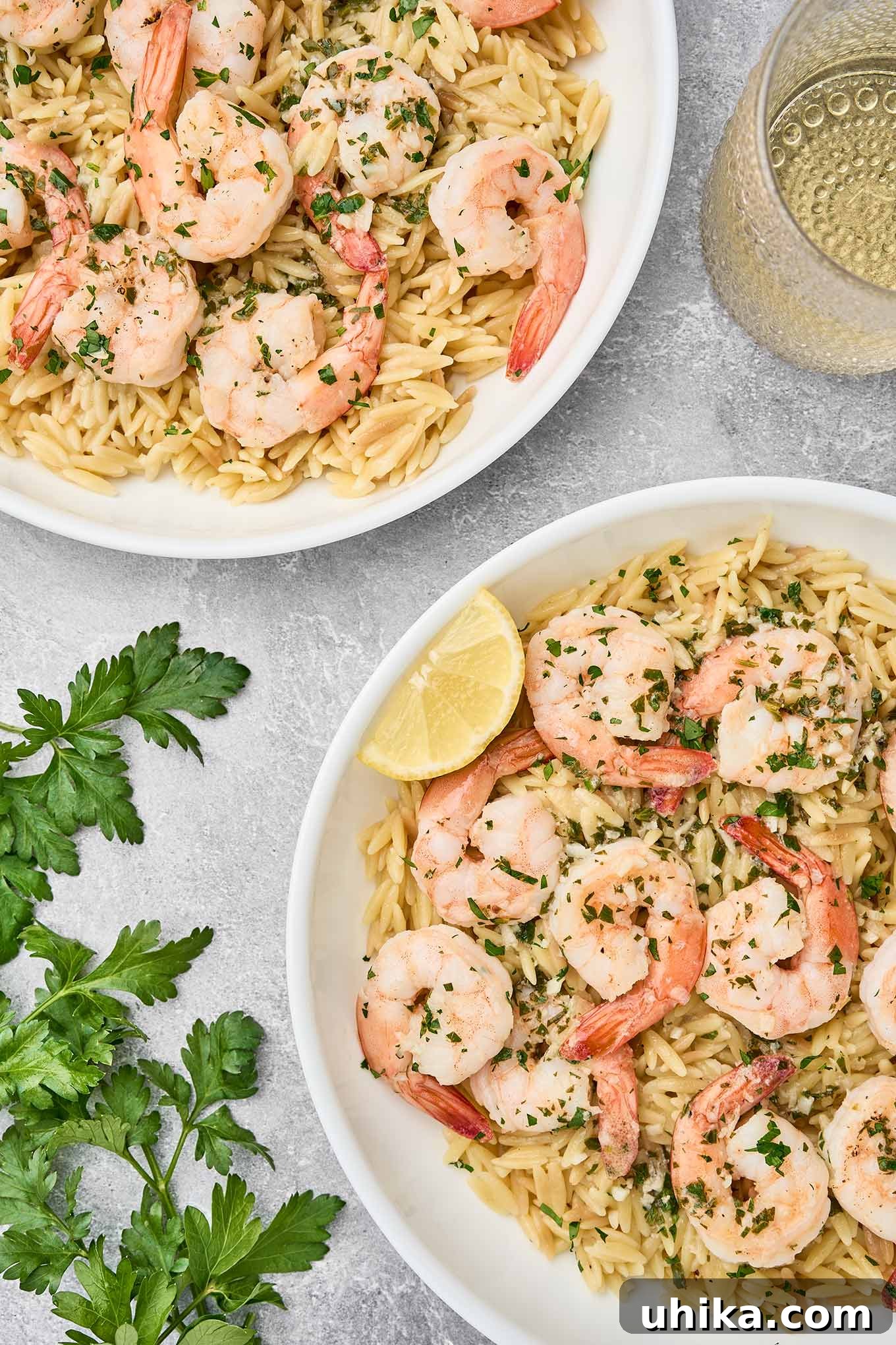 Shrimp scampi with orzo pasta served in white bowls, garnished with parsley and lemon wedges.