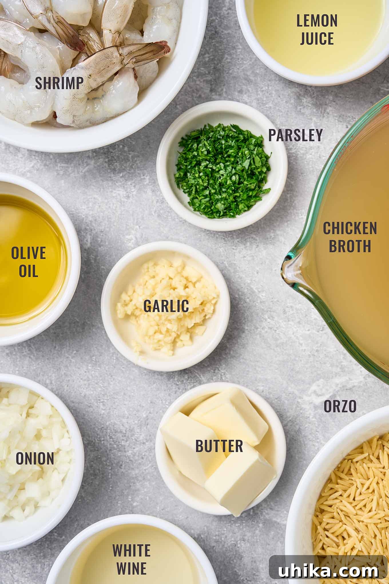 A labeled, overhead photo of the ingredients for making shrimp scampi with orzo; jumbo shrimp, orzo, garlic, butter, olive oil, onion, white with, chicken broth, lemon juice, and parsley.