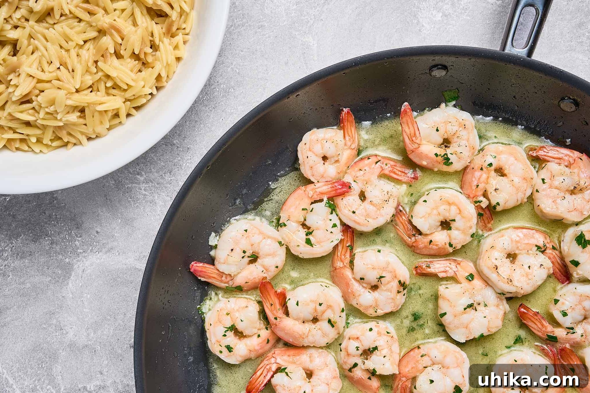 Shrimp scampi simmering in garlic butter sauce, next to a bowl of cooked orzo ready for plating.