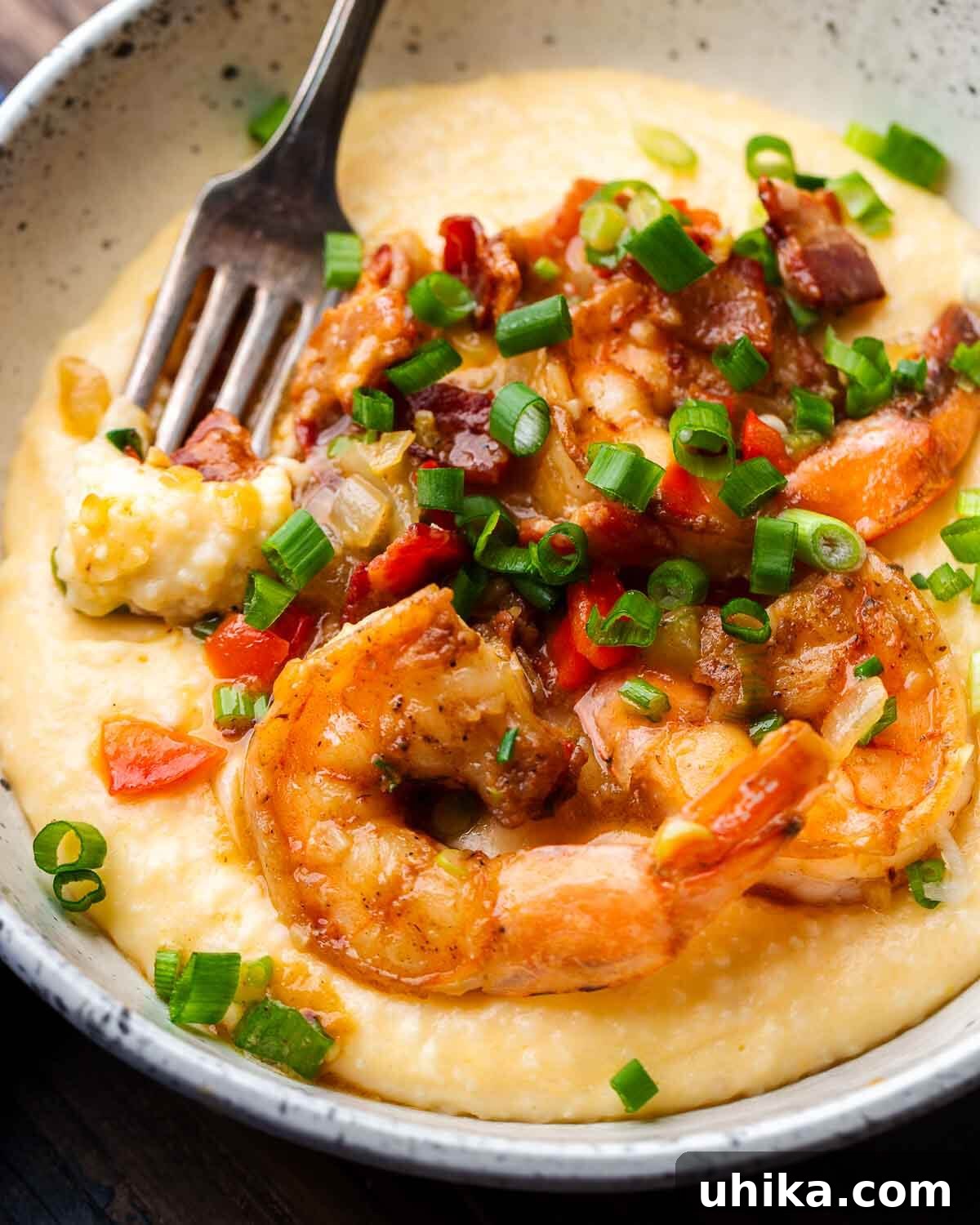 Southern Comfort Shrimp and Grits 7 A close-up of creamy shrimp and grits in a white bowl, with a fork gently dipped into the rich, cheesy grits, highlighting the inviting texture of the dish.