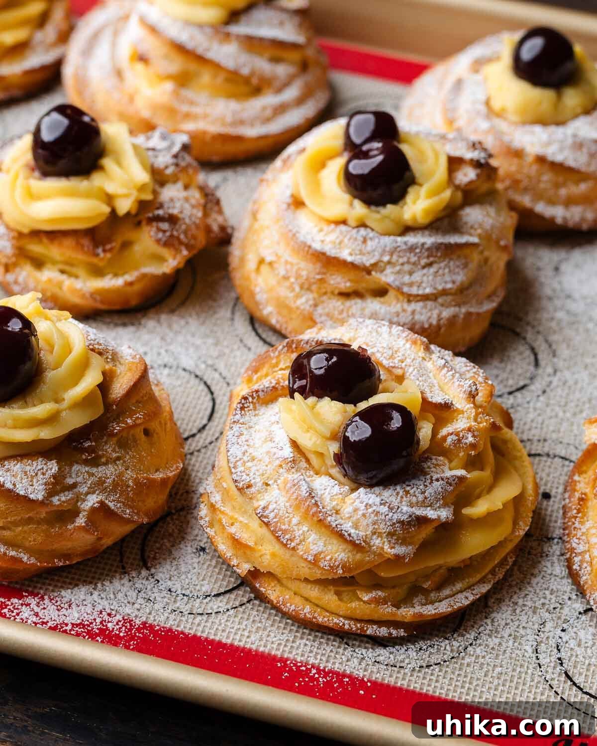 St. Joseph's Day Zeppole 2 A bunch of freshly made Zeppole di San Giuseppe pastries arranged neatly on a baking sheet, showcasing their golden-brown shells, creamy filling, and bright red Amarena cherries on top.