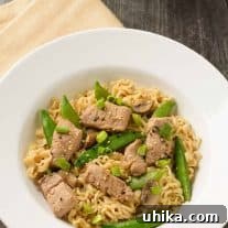 A shallow bowl of ramen noodles tossed with stir-fried pork, sugar snap peas, and scallions in soy-ginger sauce.