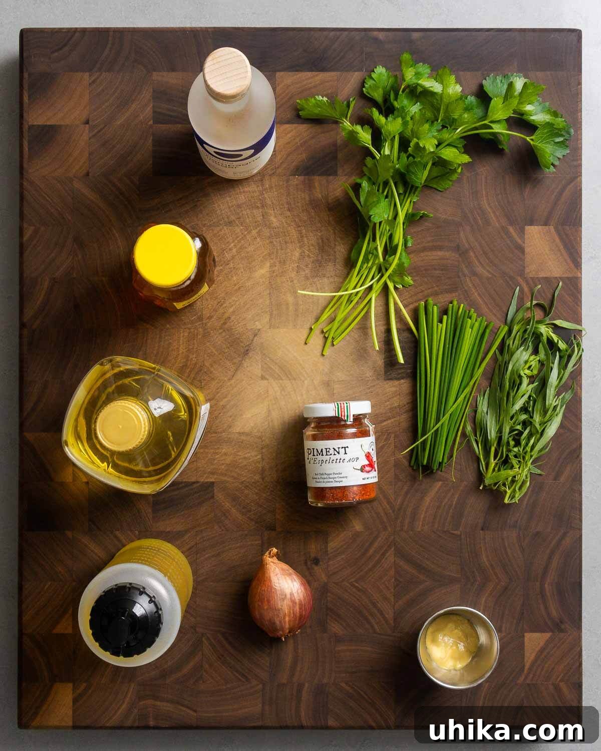 All ingredients for the French vinaigrette laid out on a clean surface, including champagne vinegar, honey, sunflower oil, olive oil, Piment d'Espelette, shallot, Dijon mustard, parsley, chives, and tarragon.