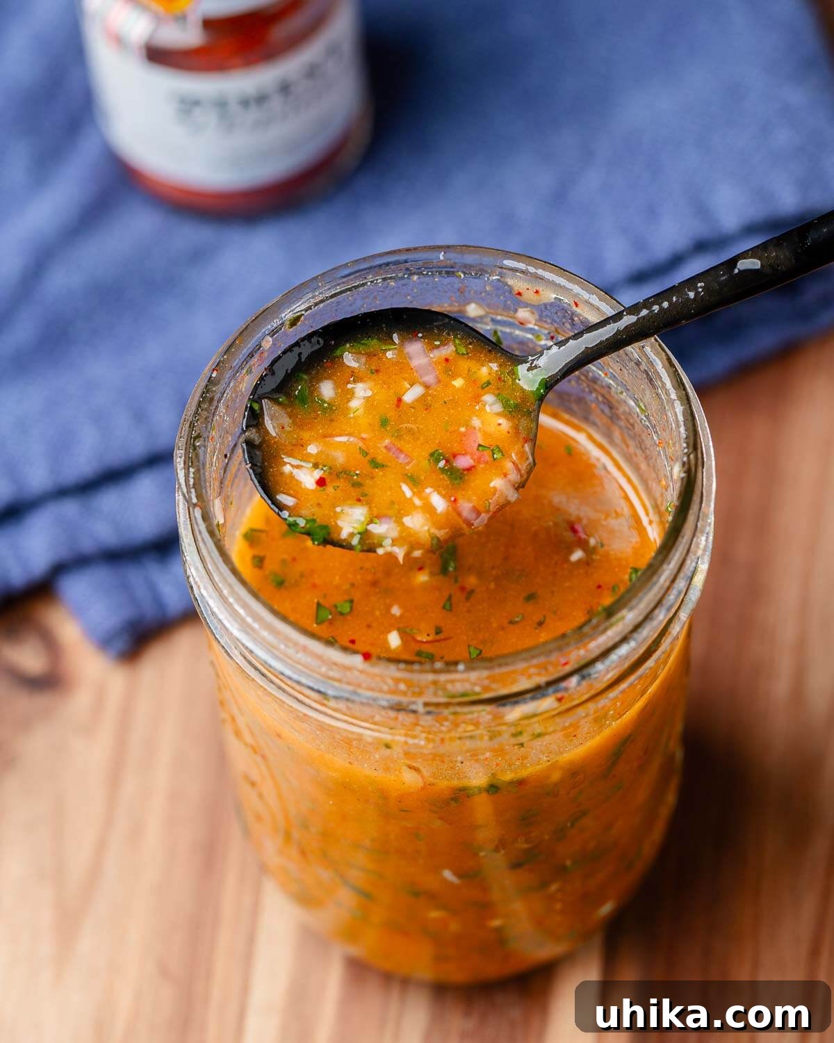Close-up shot of a spoonful of homemade French vinaigrette being poured from a mason jar, highlighting its rich texture and the fresh herbs within.