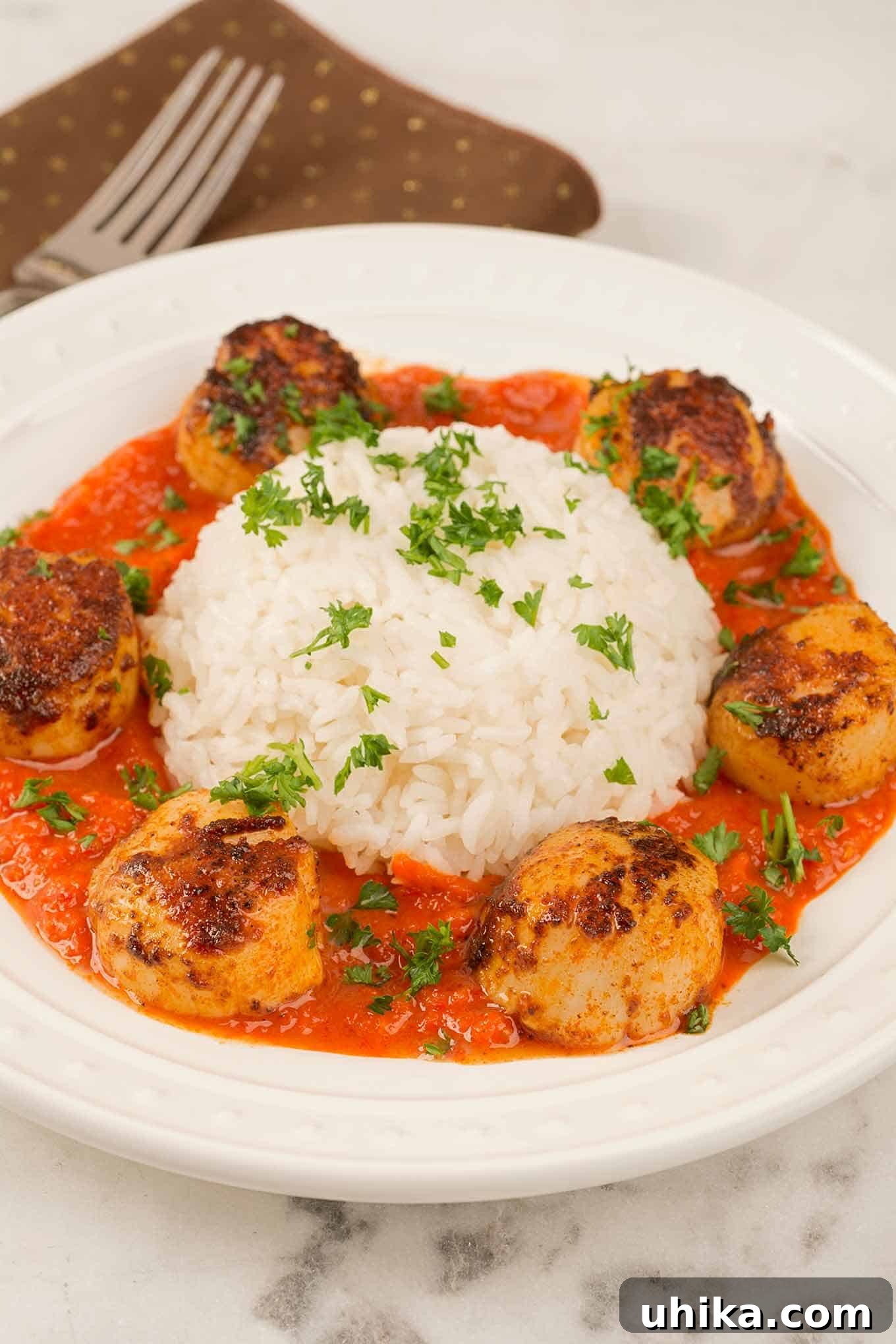 Perfectly Seared Scallops, Smoky Red Pepper Puree 2 A plate of paprika-crusted, pan-seared sea scallops in roasted red pepper sauce arranged around a serving of white rice, all garnished with chopped parsley.